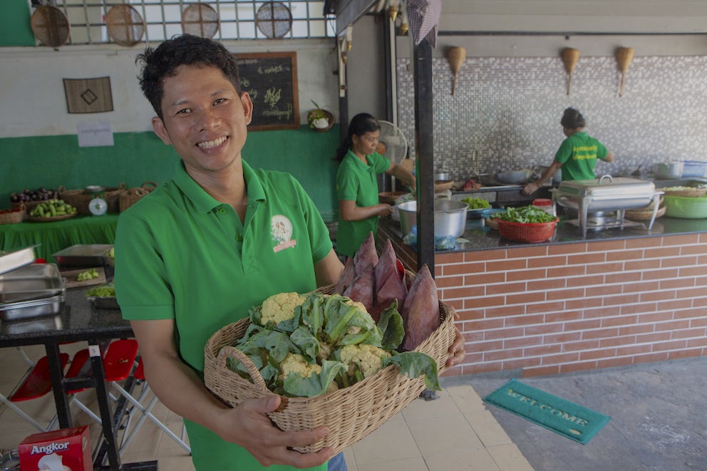 A gentleman in a green collared shirt stands with a basket of recently harvested vegetables.