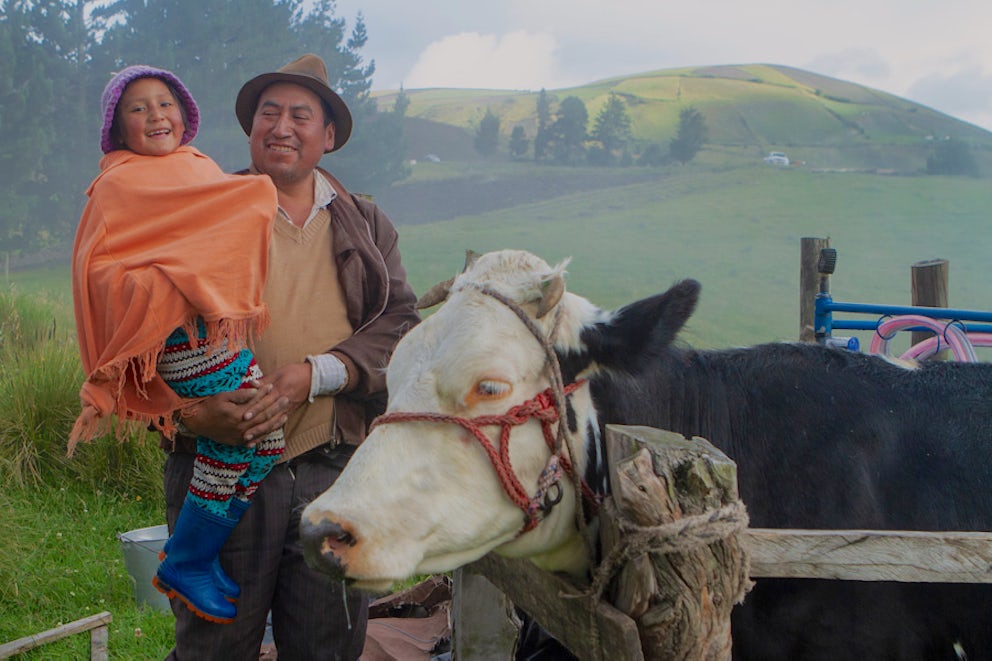 man smiling while holding his daughter and standing next to their cow