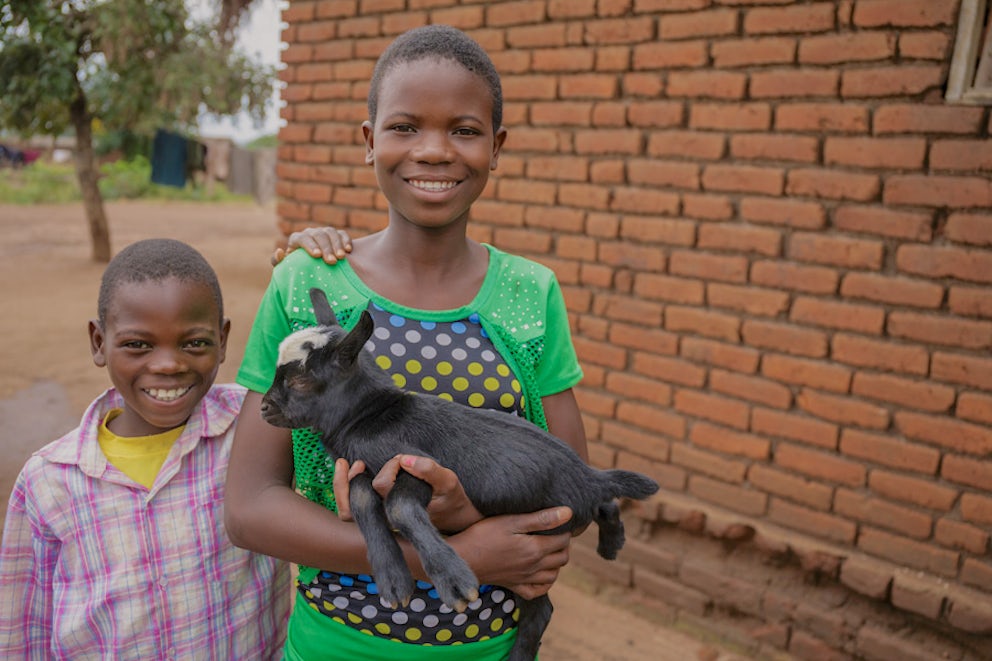two children standing next to each other, one of them is holding a baby goat