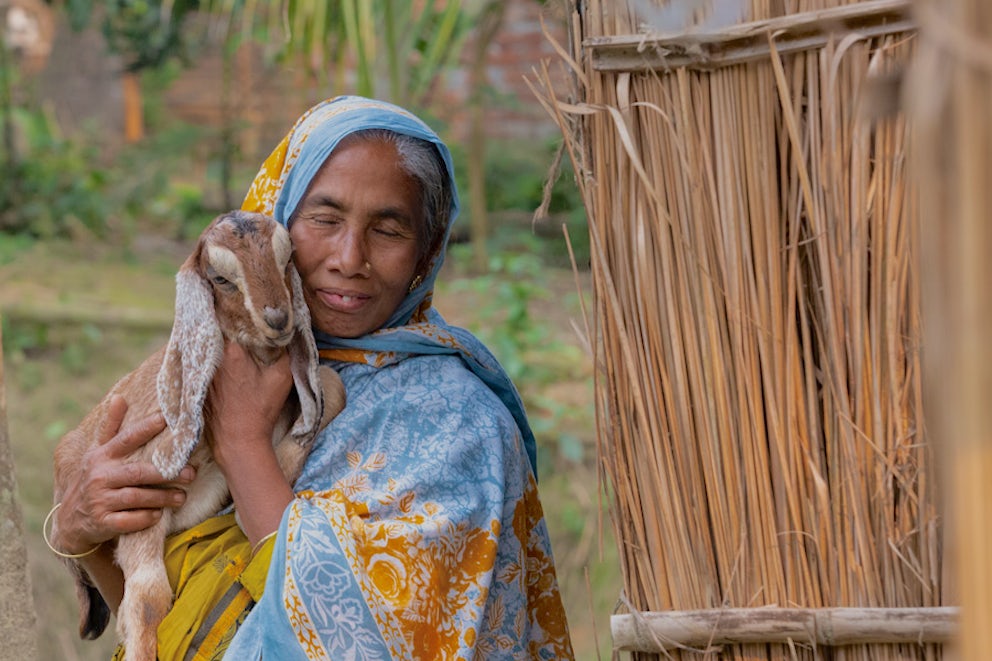 woman lovingly holding a goat up to her cheek and smiling