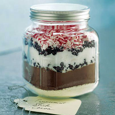 Mason jar filled with layered ingredients for hot chocolate with marshmallows and candy canes.