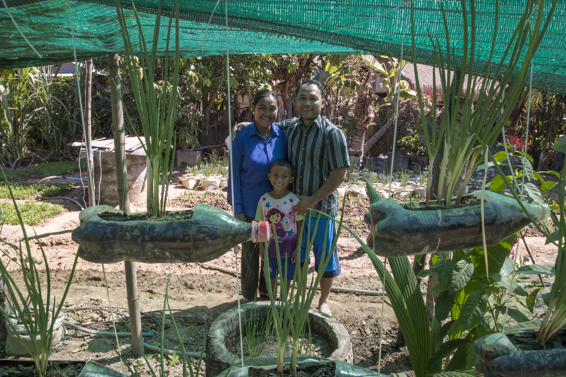 Klang Savuth, Kid Moa and Ky Damkoeung, their youngest of two sons, stand in front of their garden in Kok Komeat, Cambodia. Photo by Omar Havana.