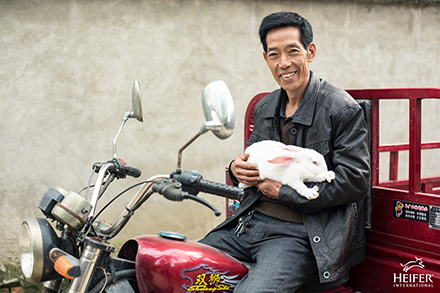 A man on a motorcycle holding a rabbit.