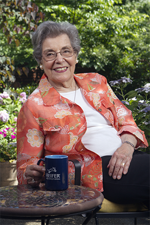 Madge Brown sits on a chair, drinking from a Heifer mug.