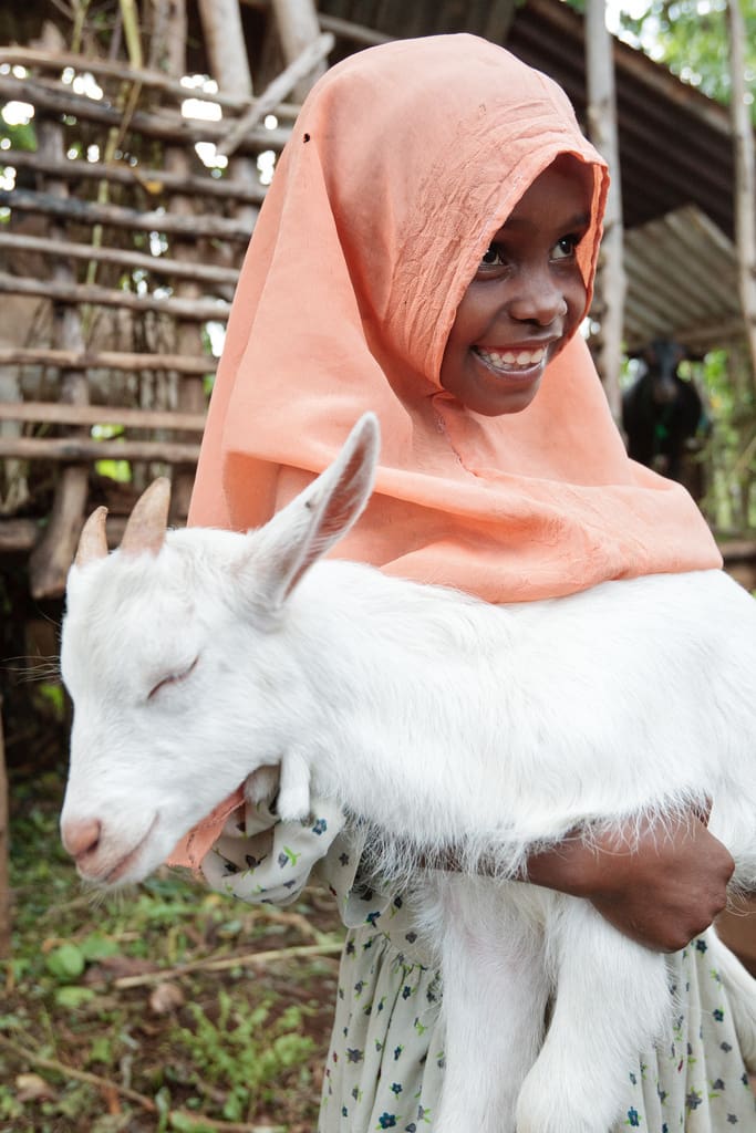 A young girl grins and holds her goat.