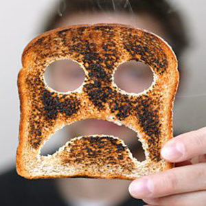 A piece of burnt toast with holes making a sad face.