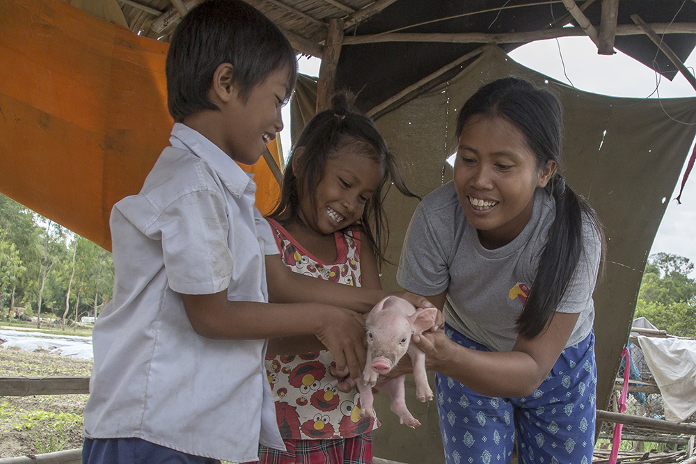 Ou Kongkea (29) (right) shows her children, Vatu Samady (7) (left) and Vatu Somavatey (5) (center), how to hold a piglet inside a pig sty set up outside the family home on December 05, 2015, in Svay Thom, Cambodia.