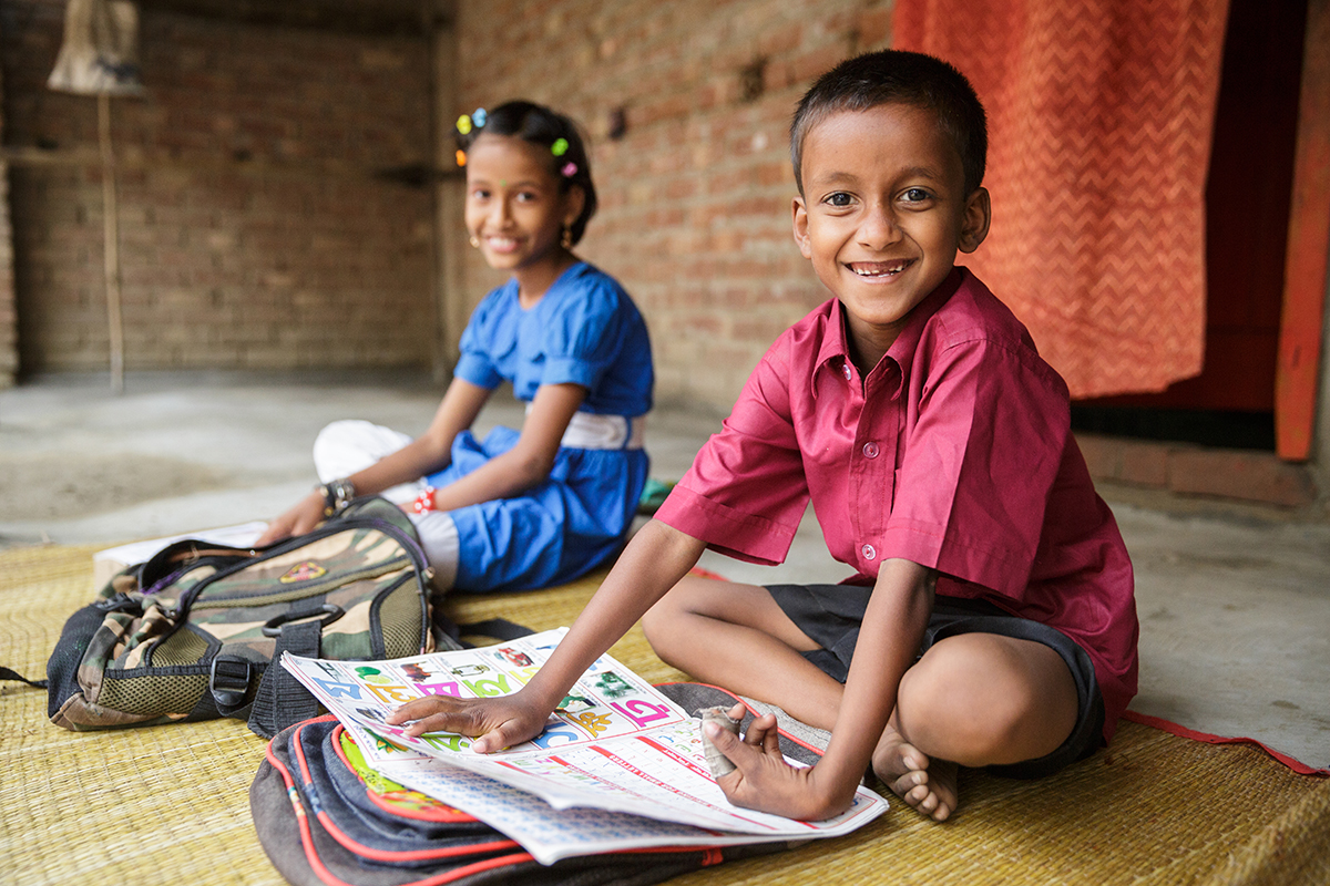 Two young students smile as they sit outside and do their homework.