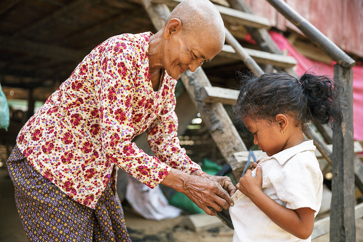 A grandmother helps put on her granddaughter's school uniform.