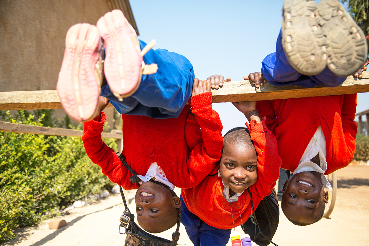 Three young students play on a playground, two swinging upside down.