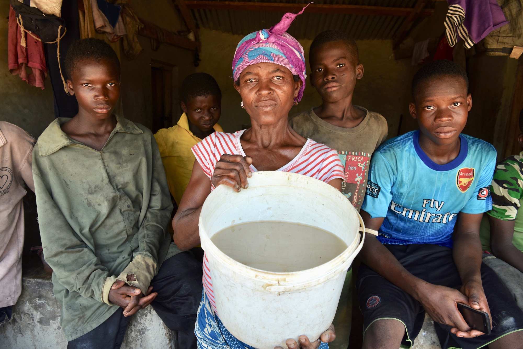 Akua Jielta with four of her children holds a bucket of dirty water.