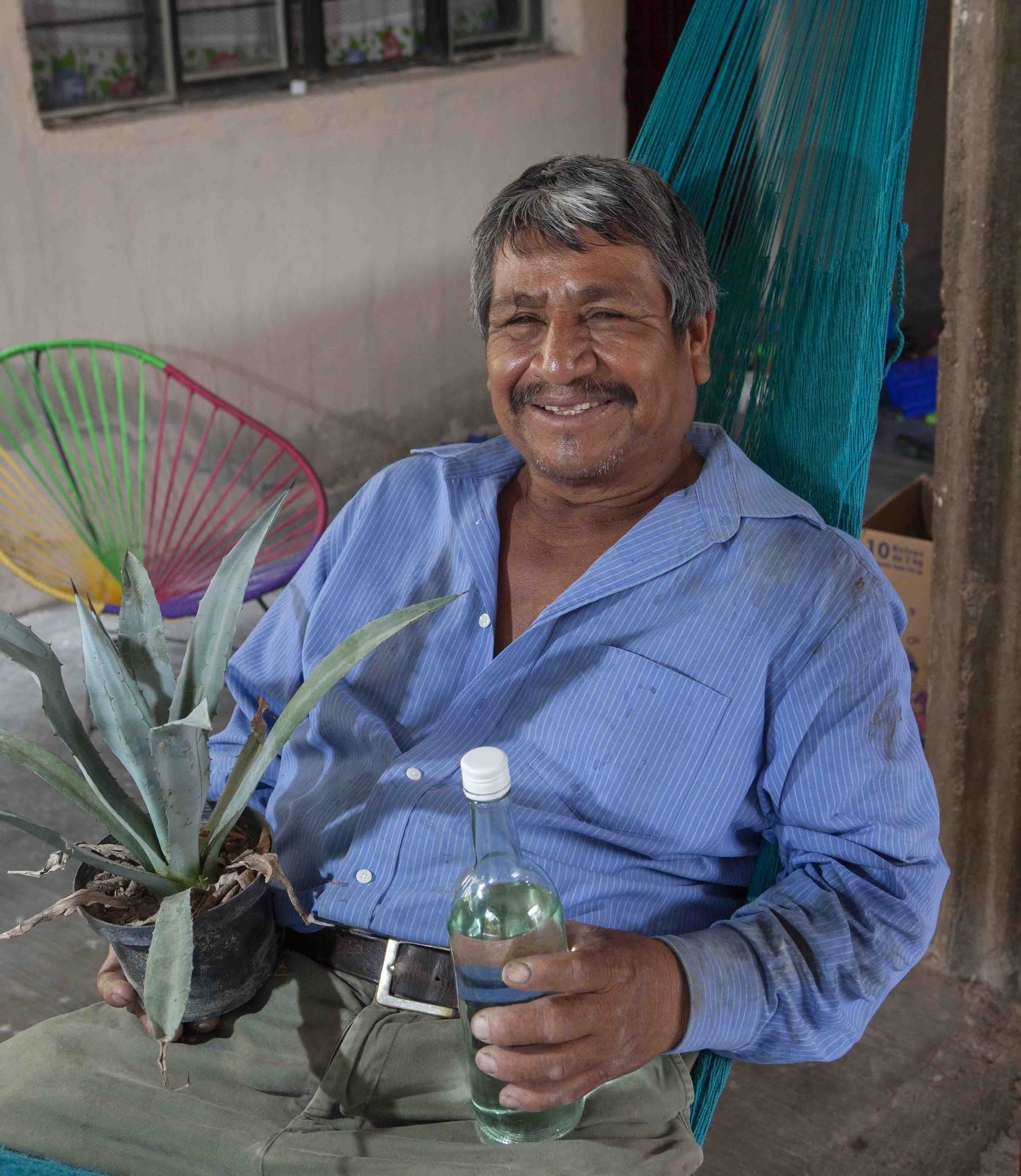 Ciro Rodriguez holds an agave plant and a bottle of mezcal produced from his crop. 