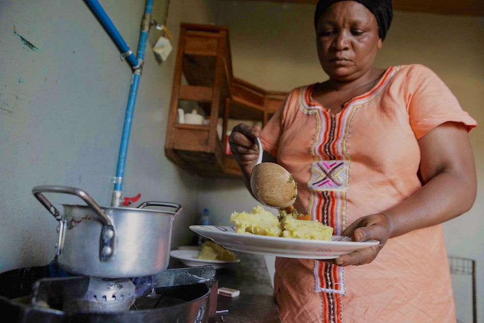 Zaina Muyabo, 49, warms up a meal for her children using a burner that runs on biogas from their cow manure digester.