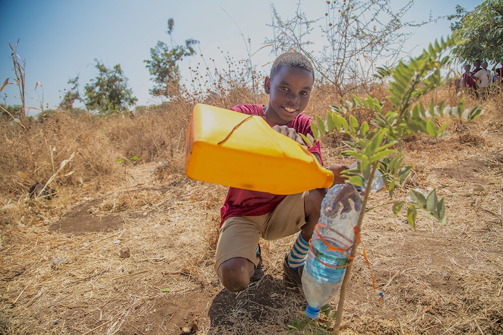 Frederick watering one of the young trees on campus with water he brought from home. Each day, every student at Jitegemee Primary School brings 5- Liters of water from home so that the trees can thrive.