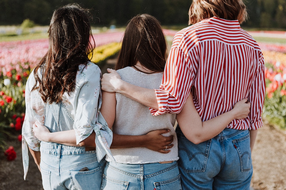 Three women with their arms around each other's backs.