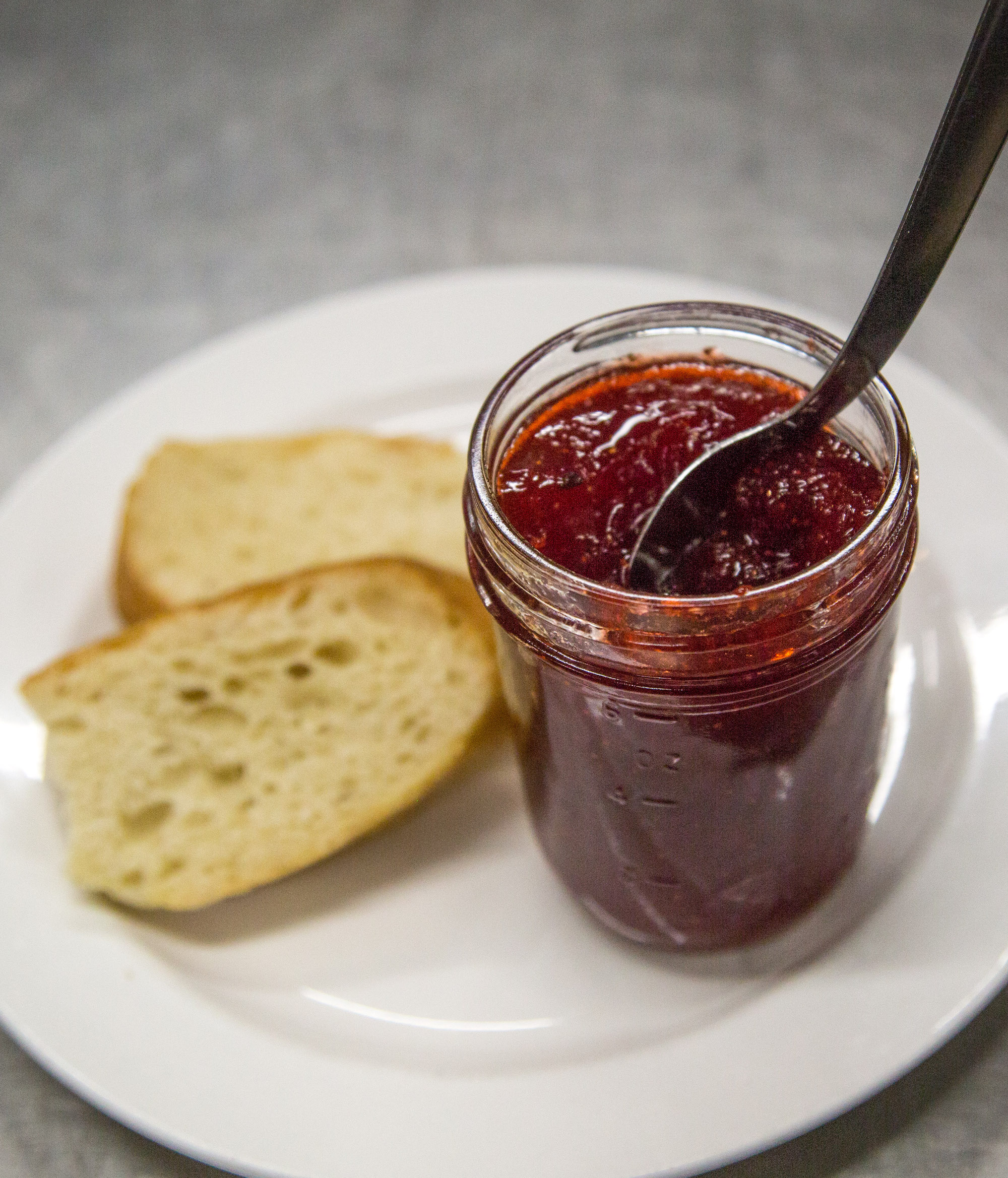 An open jar of strawberry jam on a plate with white bread.