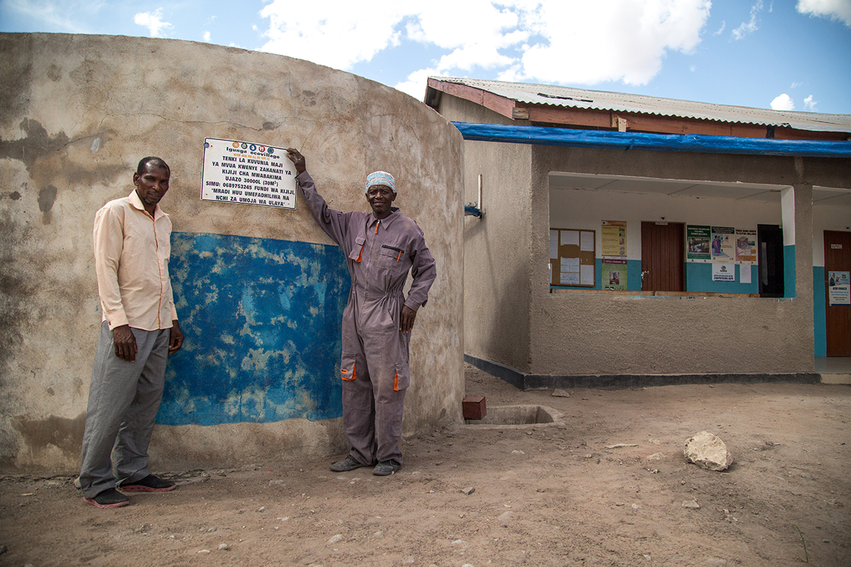 Two men proudly display their village rainwater harvesting tank.