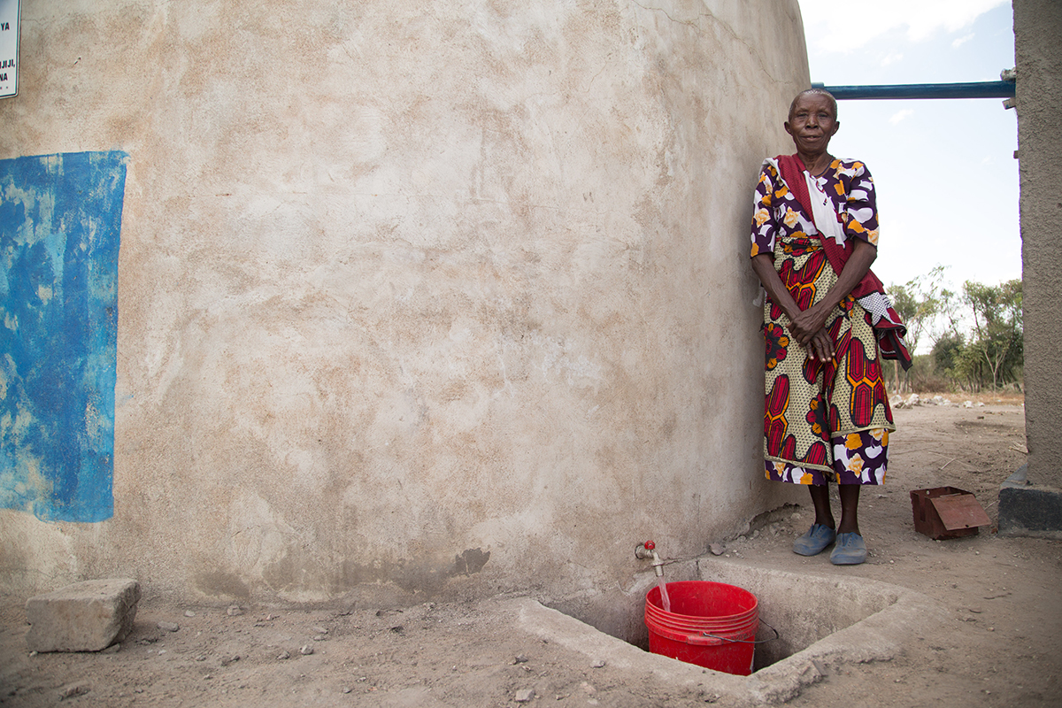 A woman stands waiting while water pours from the dispensary's rainwater harvesting tank into a bucket.