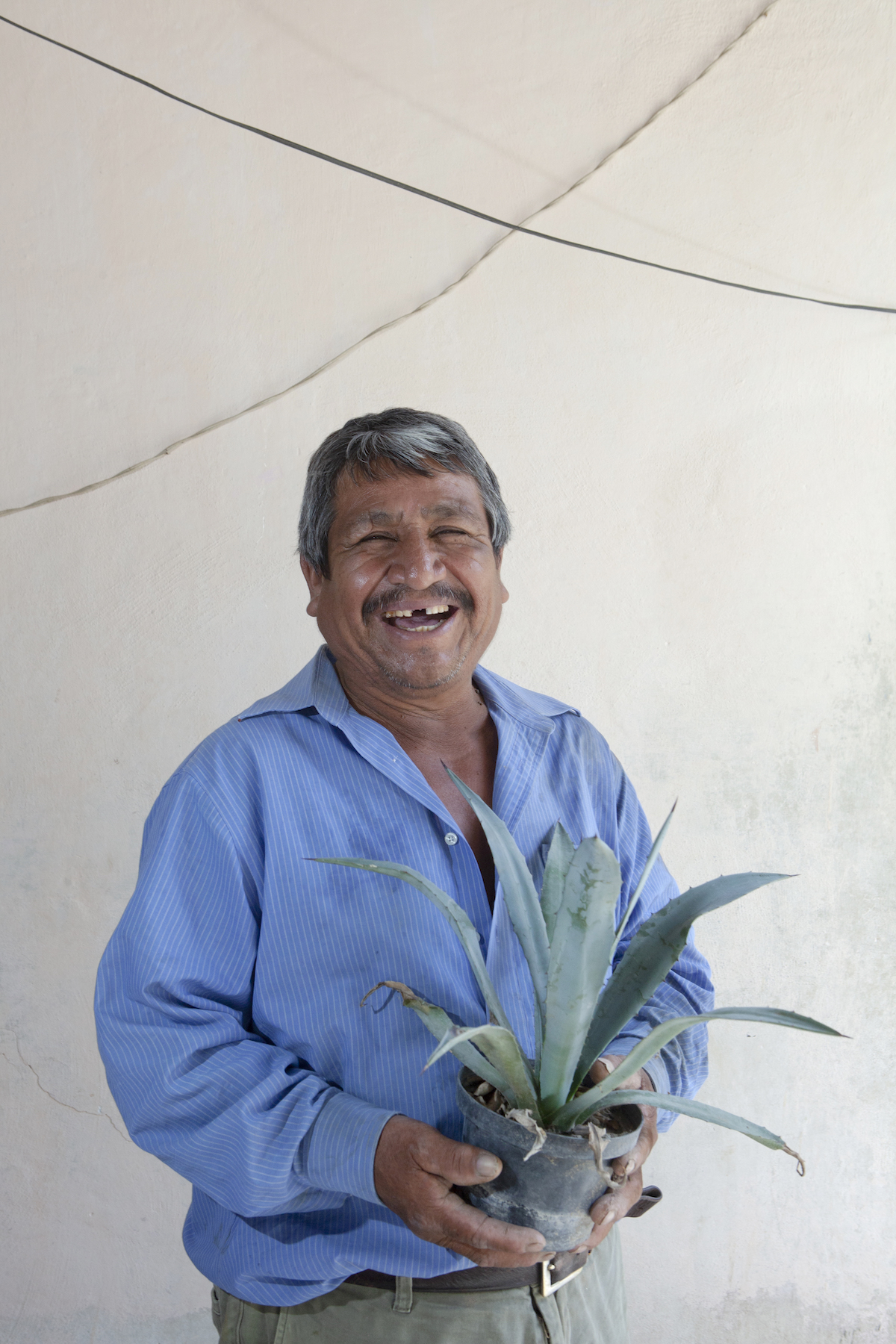 Ciro Rodriguez Cruz holds an agave plant in his home in Santa Ana del Rio. Photo by Russ Powell.