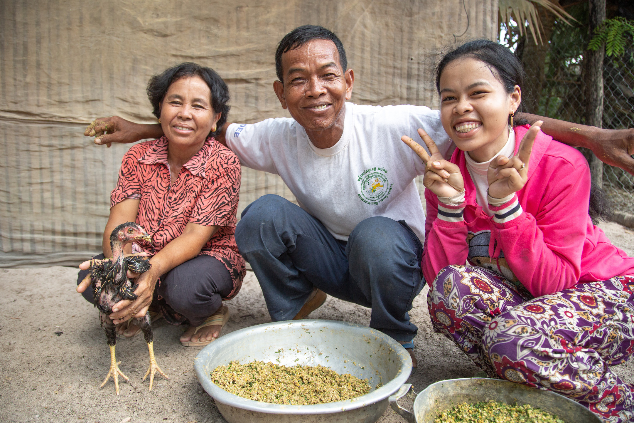 Mao Neng, her husband Prak Bon and their daughter Brak Syenech sit together smiling with a small chicken.