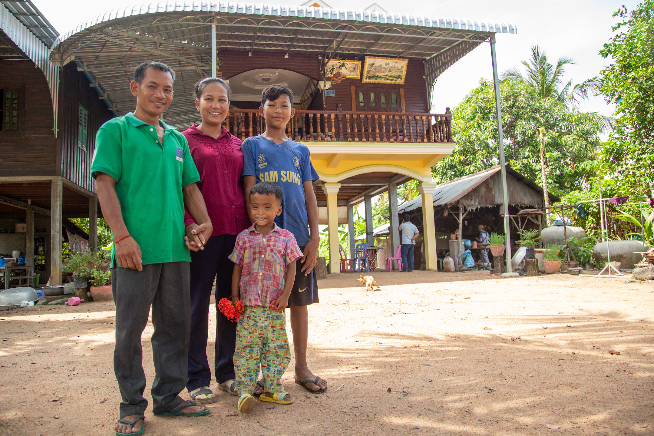 Rith Chantha, her husband, Sun Sitaol, and their two children stand smiling in front of their new home.