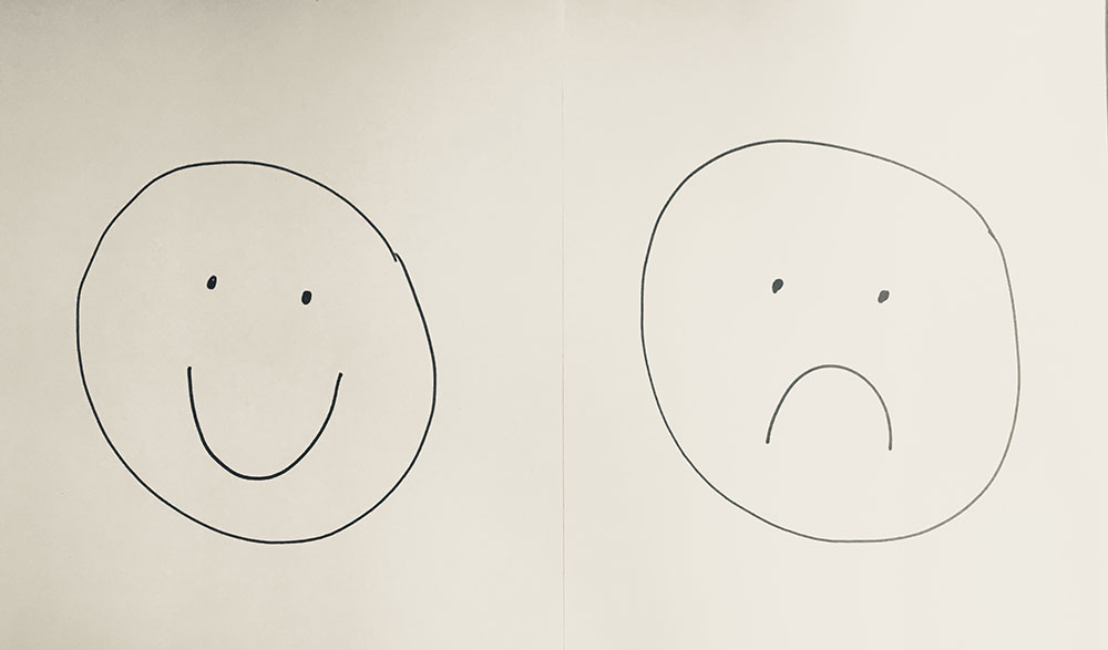 A smiley face and a frowny face drawn on paper.