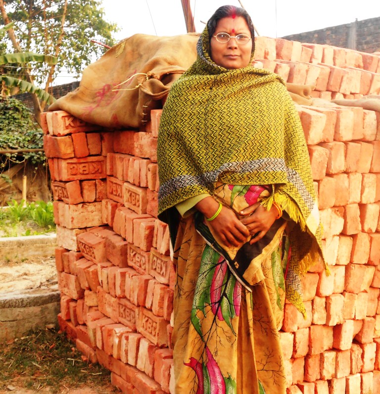 Leela Devi poses in front of Bricks she has bought for the construction of a concrete house for her family.