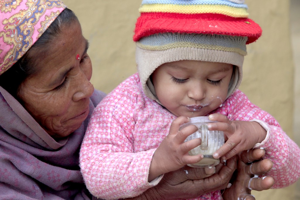 Bhumi Kumari Kathait, 49, helps her 18-month-old grandson Hemanta Bhadhur Kathait drink a cup of milk in the F Village, Nepal 
