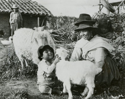 In a historical photo, a boy hugs a goat while a woman looks on