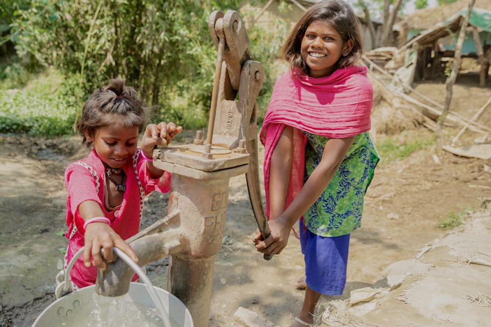 A mother and child work together to pump clean water into a bucket.