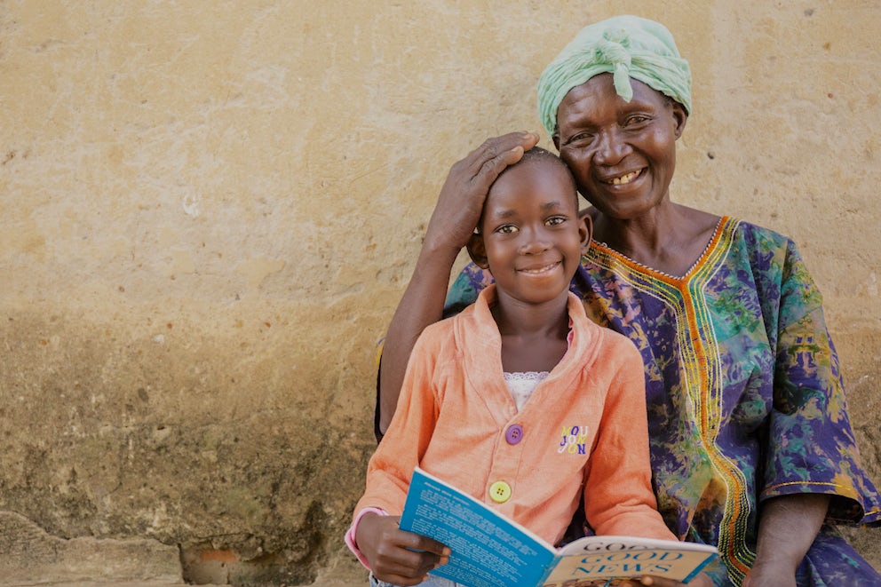Child reads to grandmother as they sit together outside their home