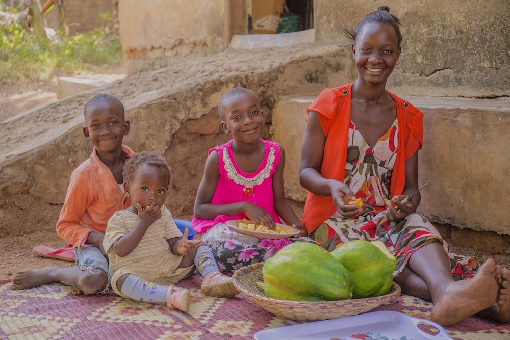  Irene sits with her daughter Michelle (center) and nieces Atim and Elisabeth as they share a papaya Irene just harvested from one of the family's trees.