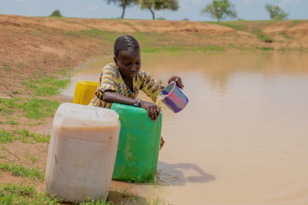 Child collects water from a big puddle from rain fall near her village.