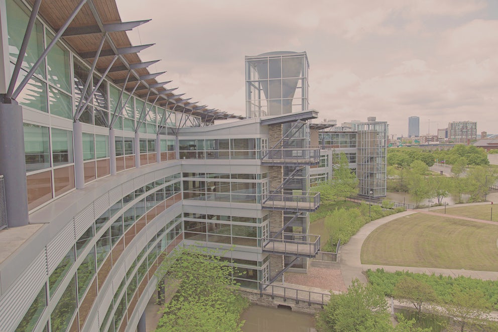Heifer Headquarters, a glass and steel building, curves around wetlands and a manicured lawn with buildings in the downtown Little Rock area in the distance.