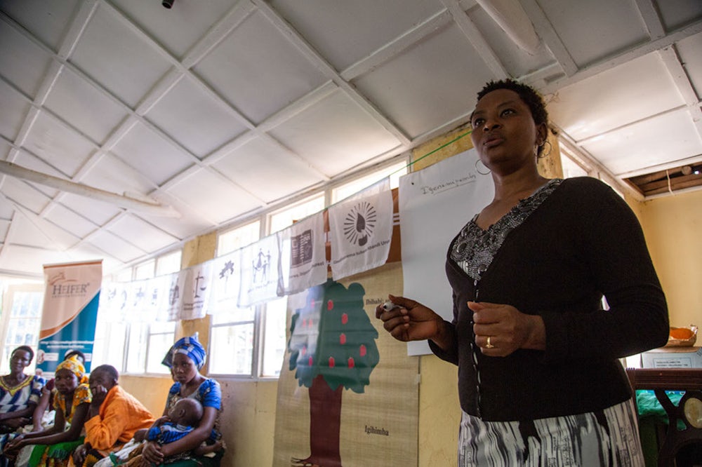 A woman in a sun-filled room in Rwanda talks to a group of people.