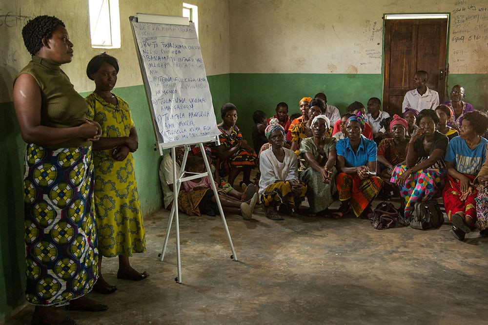 Two women in a building in Zambia present to a group of adults. 