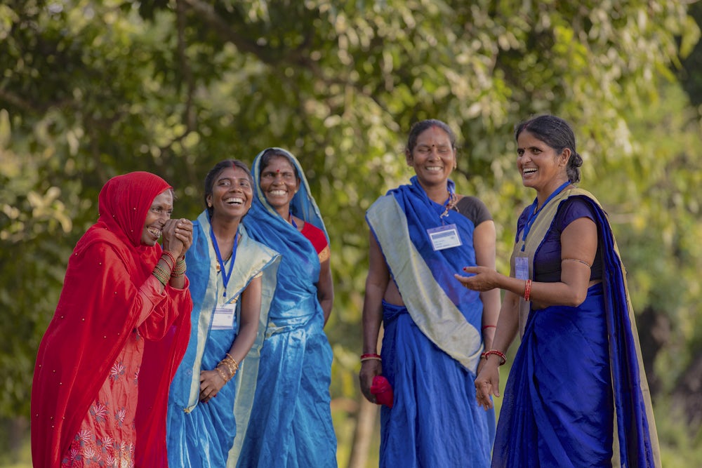 Five Indian woman wearing colorful clothing stand together, laughing.