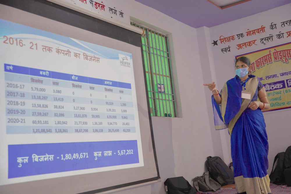 An Indian woman gives a presentation, gesturing at a screen displaying figures.