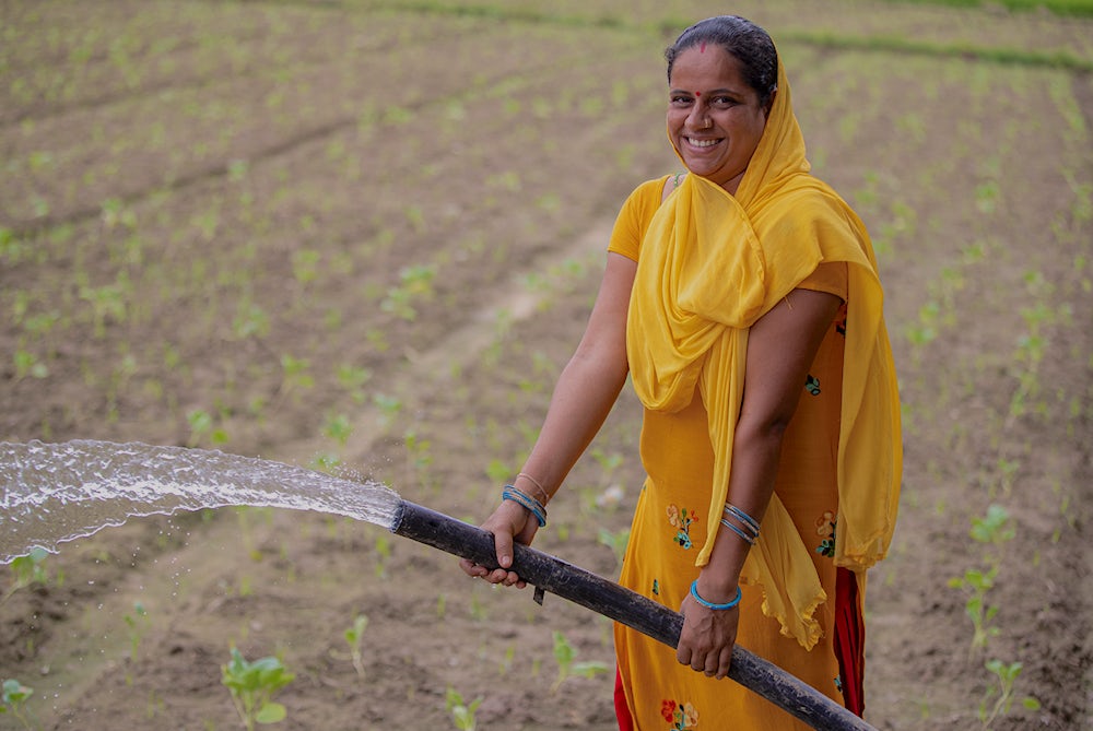 A woman sprays water from a hose on a field of vegetables.