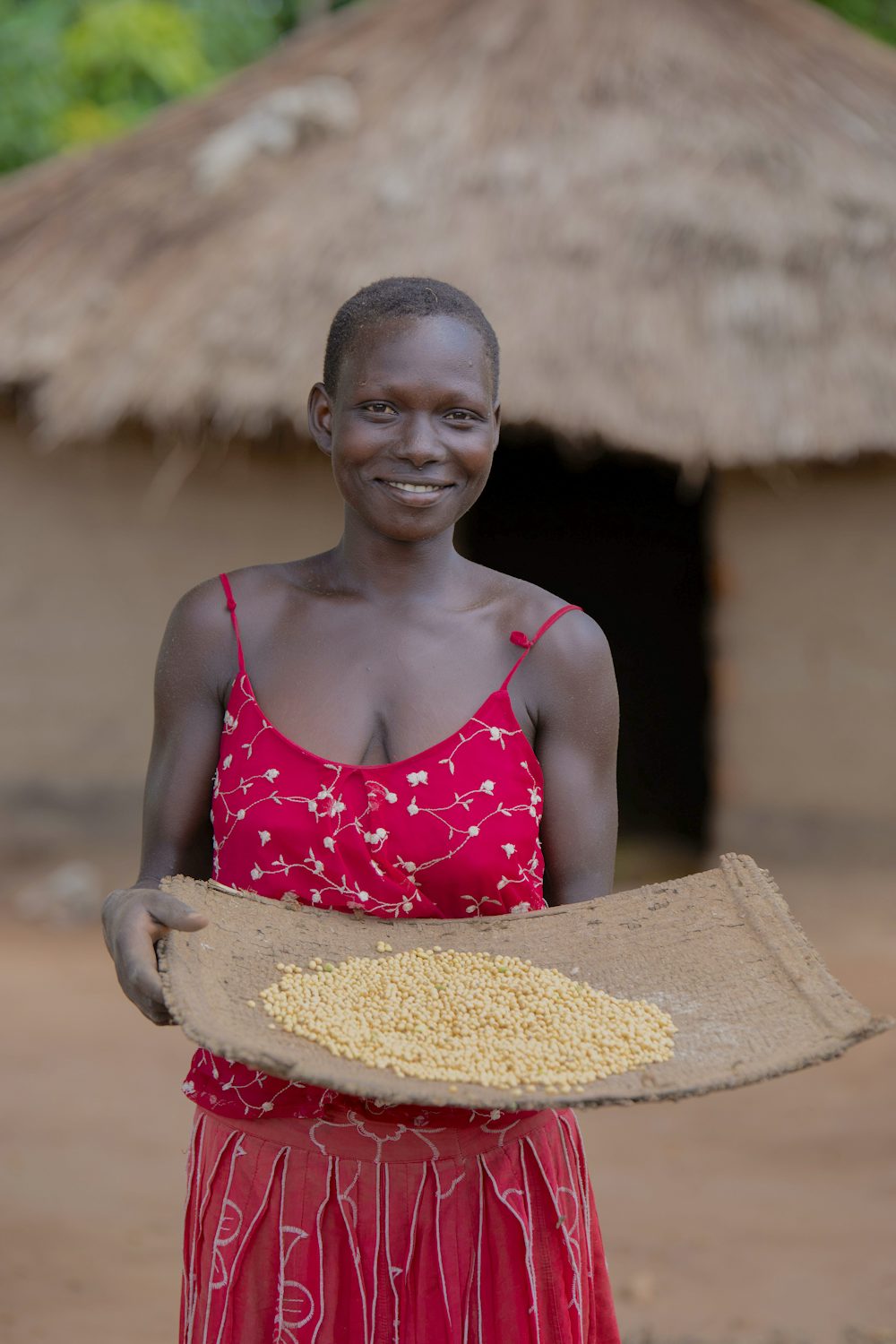 A woman poses with a tray of soybean seeds in Uganda.
