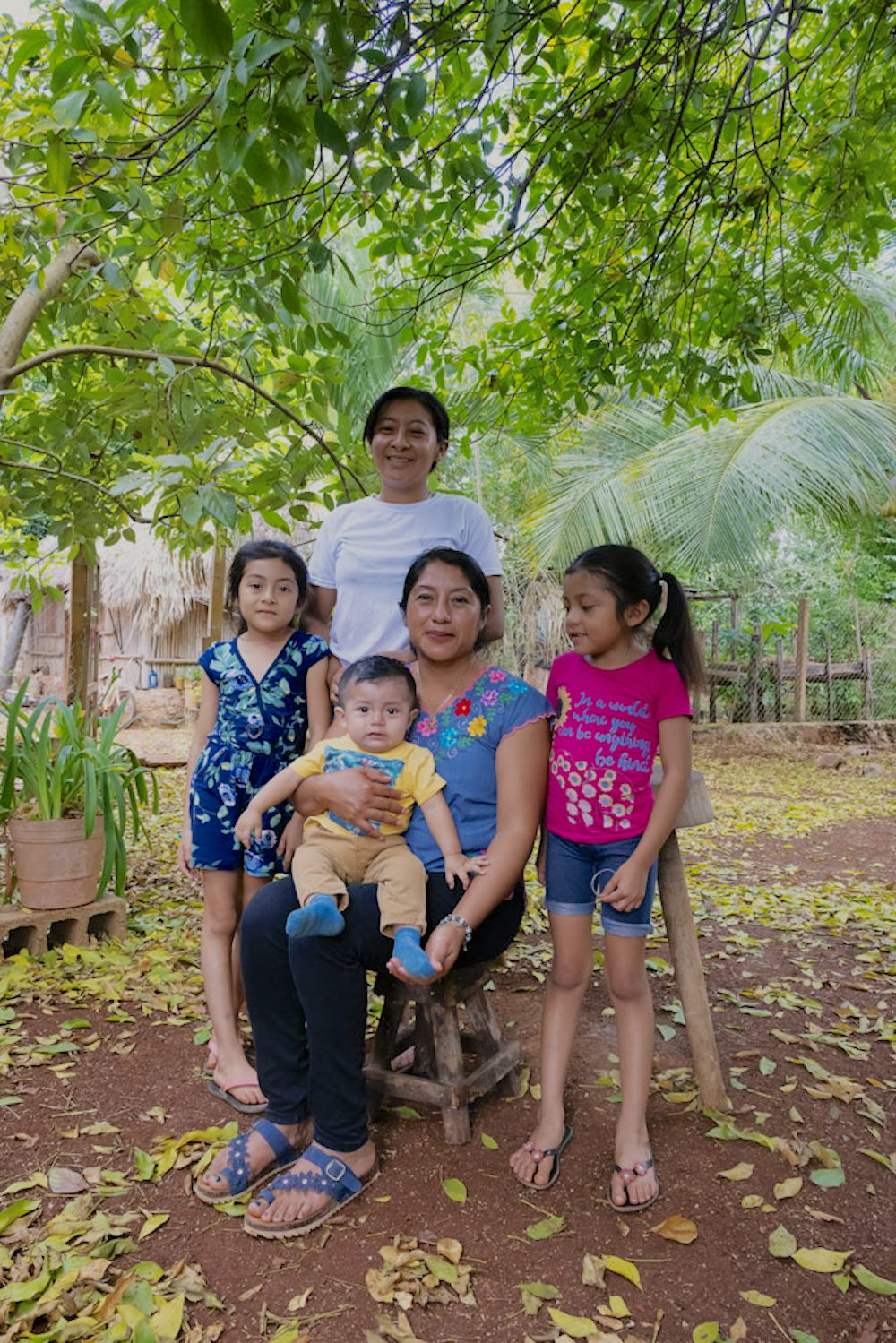 Two women and three children pose under a green tree.