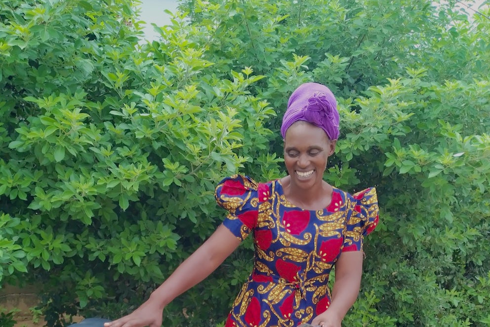 A smiling woman wearing a purple headscarf and floral dress admires her new bicycle.