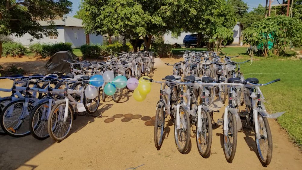 Many bikes, set to be distributed to local farmers, stand on a dirt road.