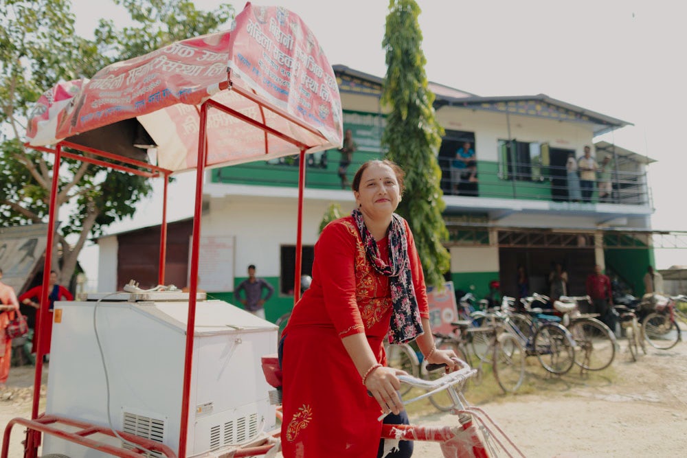 A woman riding a bike with a cooler on the back.