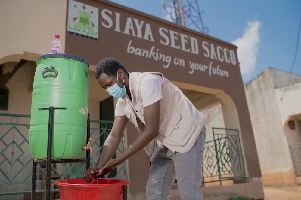 A man wearing a mask washes his hands in front of a building in Kenya.