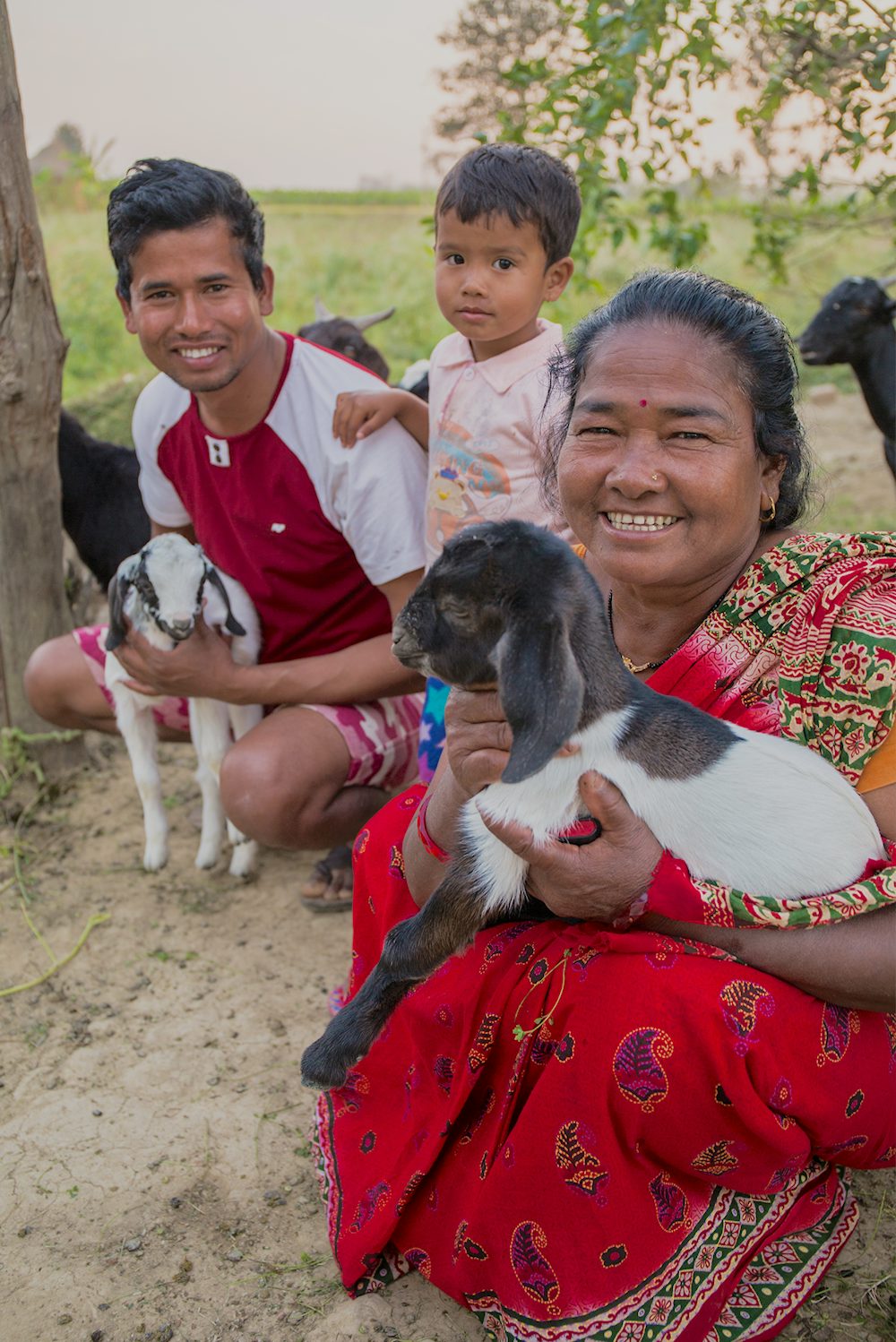 A woman, her son and her young granddaughter hold baby goats in their arms.