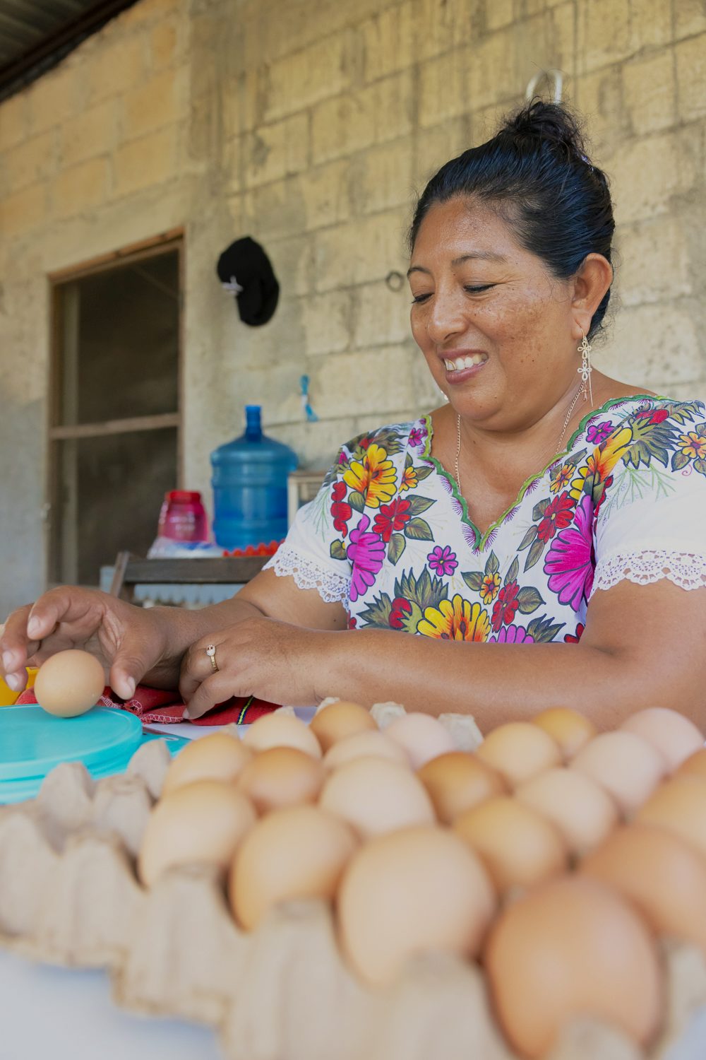 A woman sits at a table with several crates of eggs in front of her.