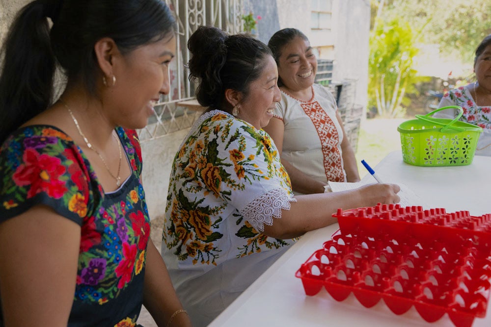 Three Mexican women sit at a table with an empty egg crate in front of them.
