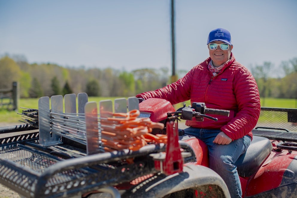 A woman wearing sunglasses and a baseball cap drives a large ATV.