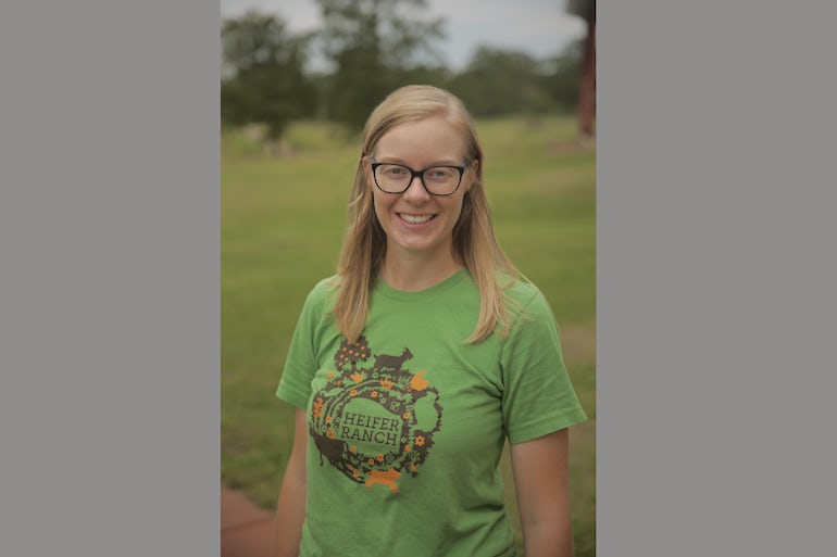 A woman in a green Heifer Ranch shirt smiles at the camera.